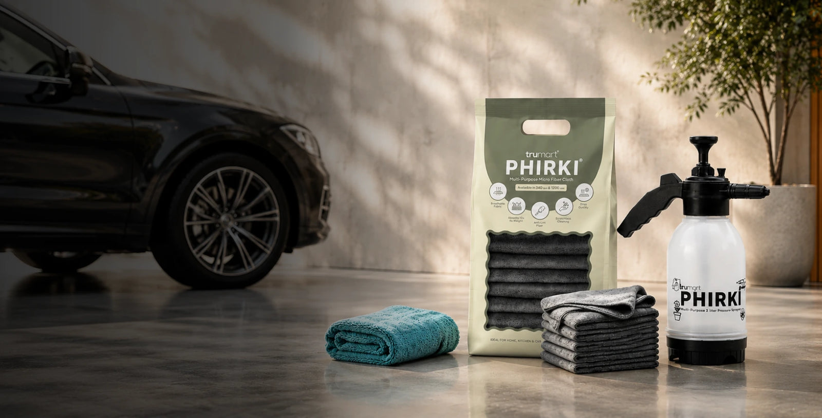 PHIRKI Car cleaning products including a 2L foam sprayer and microfiber cloths on a reflective surface with a car in the background.